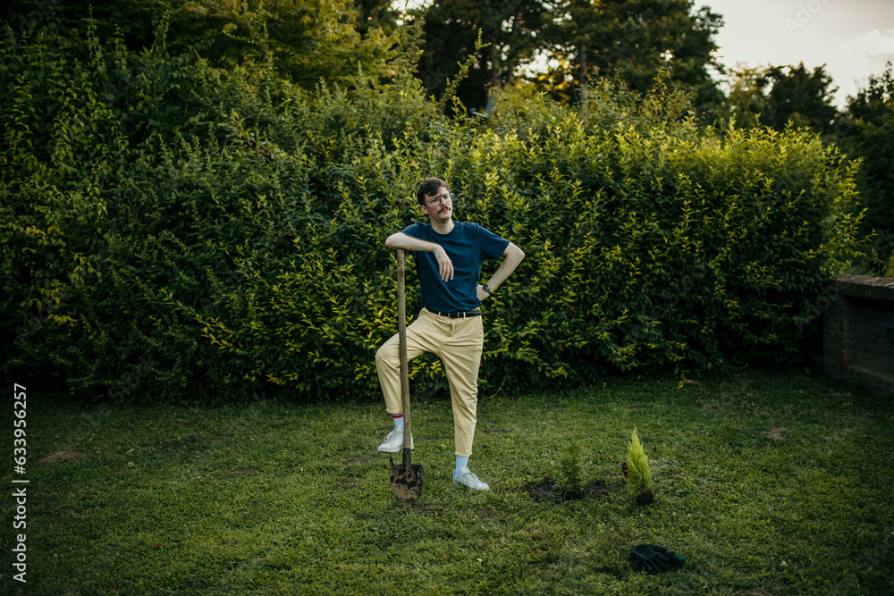 Man standing in his garden with a shovel and planting a new tree.