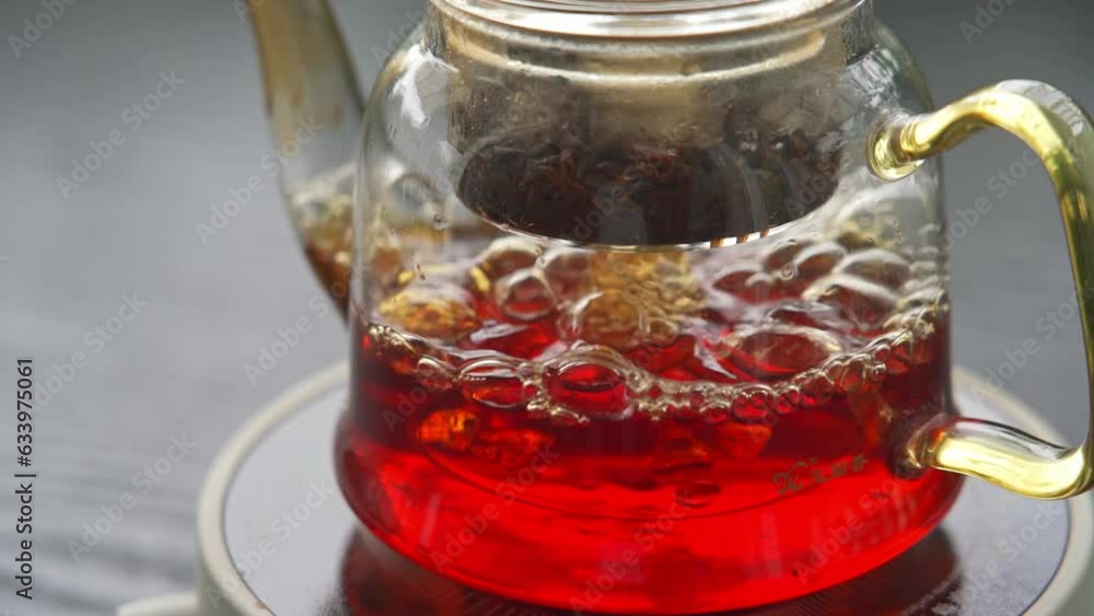 Elevated slow motion of black tea brewing in glass teapot on electric stove in garden Elevated slow motion of black tea brewing in glass teapot on electric stove in garden