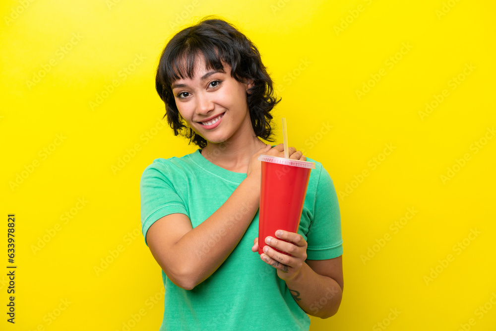 Young Argentinian woman holding a soda isolated on yellow background laughing Young Argentinian woman holding a soda isolated on yellow background laughing