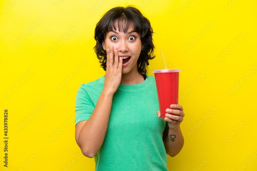 Young Argentinian woman holding a soda isolated on yellow background with surprise and shocked facial expression Young Argentinian woman holding a soda isolated on yellow background with surprise and shocked facial expression