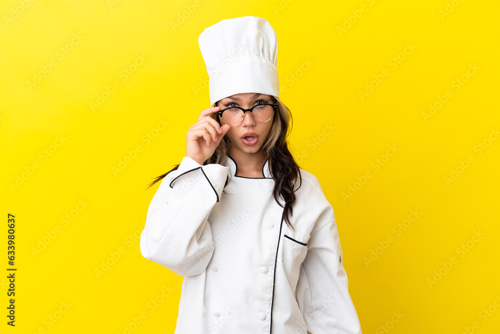 Young Russian chef girl isolated on yellow background with glasses and surprised Young Russian chef girl isolated on yellow background with glasses and surprised