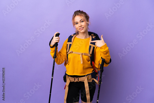Teenager girl with backpack and trekking poles over isolated purple background proud and self-satisfied