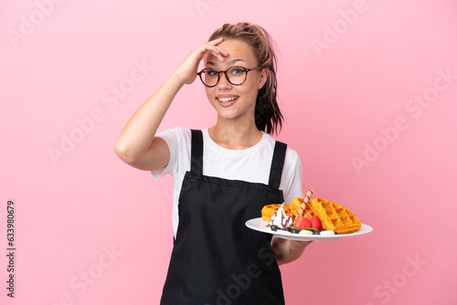 Restaurant waiter Russian girl holding waffles isolated on pink background doing surprise gesture while looking to the side