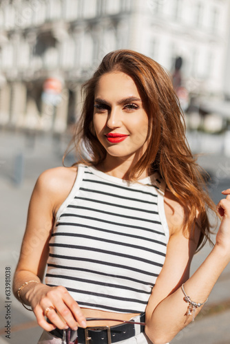 Beautiful happy fashion girl with red lips walking in the city on a sunny summer day
