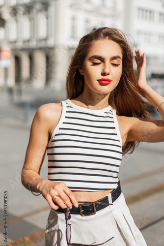Beautiful cute sensual girl model with red lips in trendy fashion summer clothes in the city on a sunny day