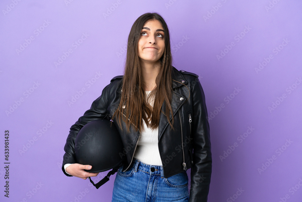 Young caucasian woman with a motorcycle helmet isolated on purple background and looking up Young caucasian woman with a motorcycle helmet isolated on purple background and looking up