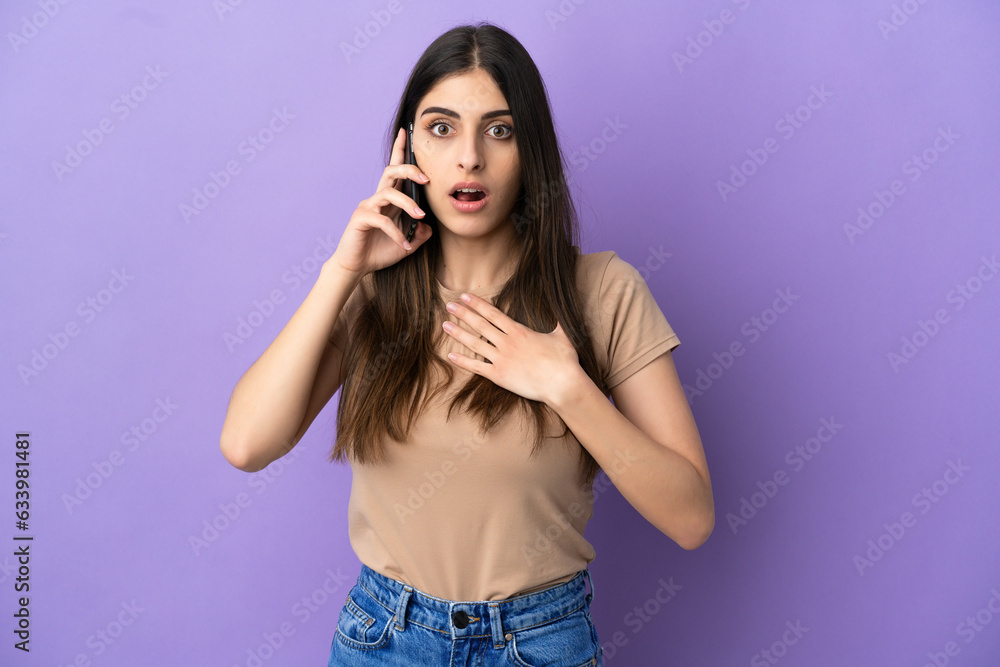 Young caucasian woman using mobile phone isolated on purple background surprised and shocked while looking right Young caucasian woman using mobile phone isolated on purple background surprised and shocked while looking right