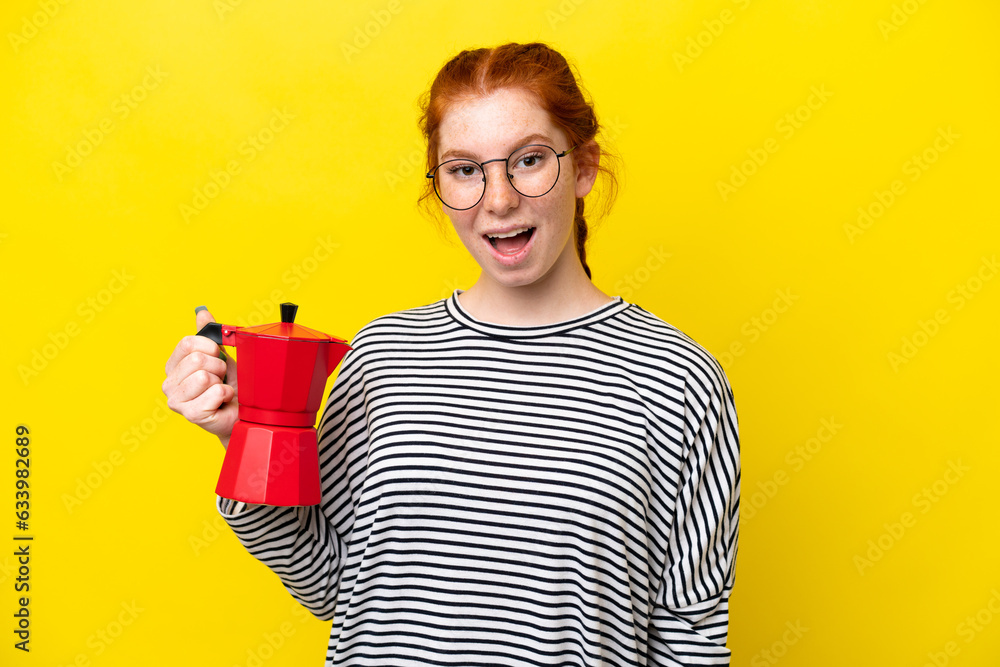 Young reddish woman holding coffee pot isolated on yellow background with surprise and shocked facial expression
