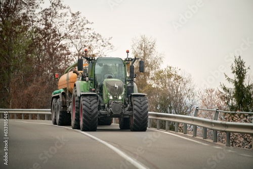 Agricultural Efforts in Motion. A Tractor at Work on a Sunny Summer Day. Farm tractor moving on the rural road near the farm