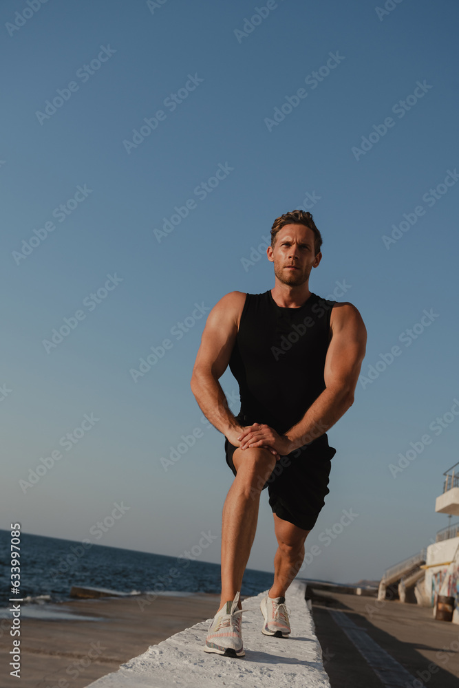 Low angle view of male athlete doing stretching exercises with the sea view on background