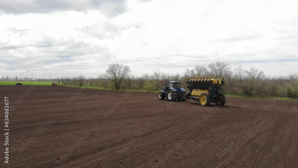 Blue tractor planting sunflower with yellow planter on the field in Ukraine Blue tractor planting sunflower with yellow planter on the field in Ukraine