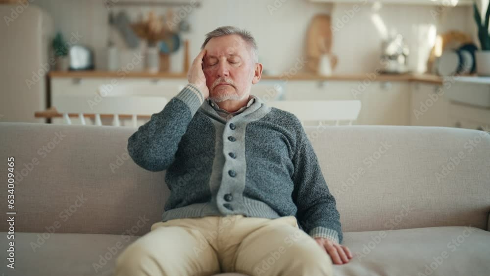 Senior man suffering from terrible headache touching head sitting on couch at home, making massage with closed eyes,doing turning head on sides exercise. Migraine, high intracranial pressure concept. Senior man suffering from terrible headache touching head sitting on couch at home, making massage with closed eyes,doing turning head on sides exercise. Migraine, high intracranial pressure concept.