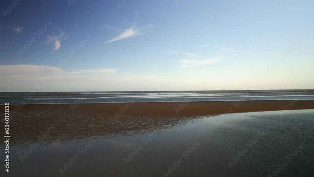 Aerial drone view of serene Australian coastline with two people walking on low tide sandy beach shore, calm water, vibrant blue sky, fluffy clouds. Peaceful tropical summer beach holiday backdrop. Aerial drone view of serene Australian coastline with two people walking on low tide sandy beach shore, calm water, vibrant blue sky, fluffy clouds. Peaceful tropical summer beach holiday backdrop.
