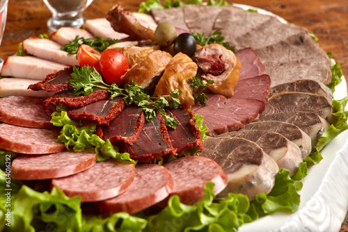 Plate with cold cuts with choice - salami, pieces of sliced ham, sausage, chicken, qazi horse meat, tomatoes on salad, close-up, shallow depth of field