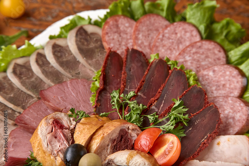 Part of plate with cold cuts with choice - salami, pieces of sliced ham, sausage, chicken, qazi horse meat, tomatoes on salad, close-up, shallow depth of field