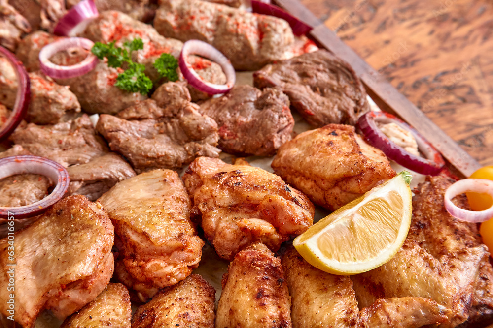 Part of the wooden board with fried meat and vegetables on the wooden table,close-up, shallow depth of field. Chicken meat and lemon in focus
