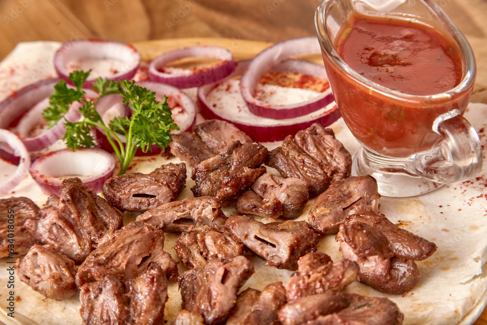 Part of the wooden board with fried beef meat with red onion rings, sauce and pita bread on the wooden table, close-up perspective view, shallow depth of field. Meat and sauce in focus