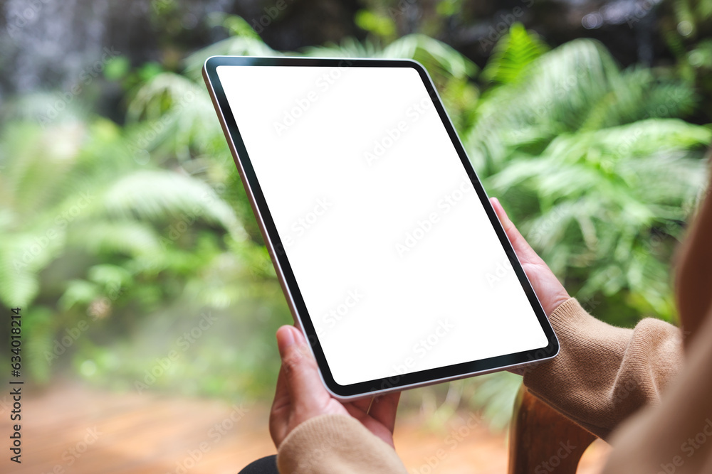 Mockup image of a woman holding digital tablet with blank white desktop screen in the garden