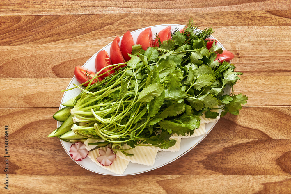 White plate with greens, tomatoes, curd cheese and radishes on the wooden table. Top view, flat lay White plate with greens, tomatoes, curd cheese and radishes on the wooden table. Top view, flat lay
