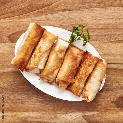 White plate with fried pita rolls with meat on the wooden table with parsley near it. Top view, flat lay