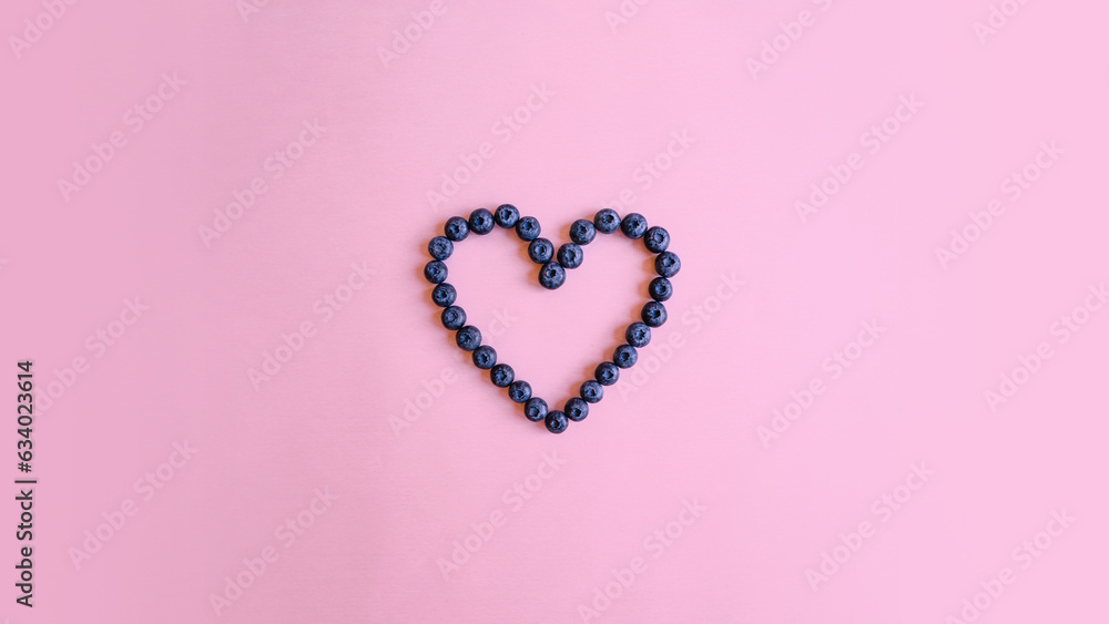 Heart made of blueberries on pastel pink background. Original blueberry decoration. Minimal summer concept. Welcome summer. Copy space.