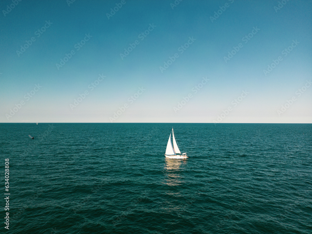 aerial view of a sailboat plowing alone in slightly rough seas. The photo conveys a sense of serenity and tranquility without forgetting the danger of the sea