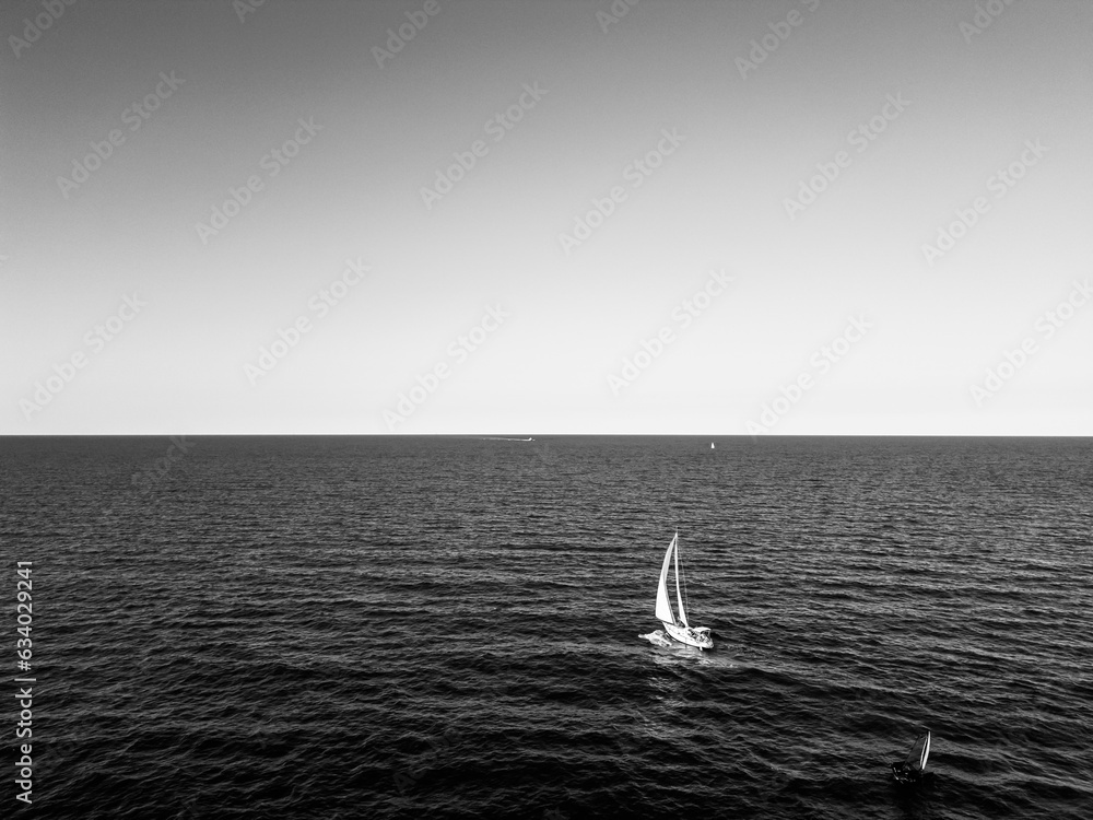 aerial view of a sailboat plowing alone in slightly rough seas. The photo conveys a sense of serenity and tranquility without forgetting the danger of the sea