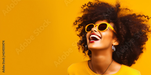 laughing young black woman with cool sunglasses isolated on a yellow background wall