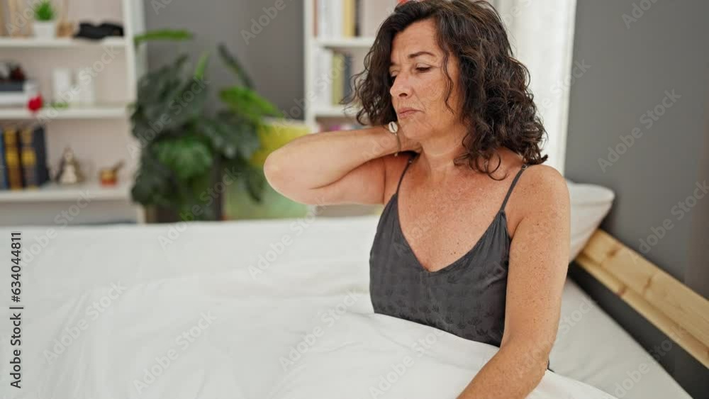 Middle age hispanic woman sitting on bed suffering for cervical pain at bedroom Middle age hispanic woman sitting on bed suffering for cervical pain at bedroom