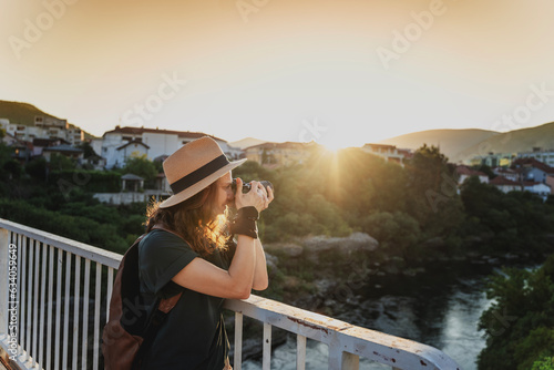 Young caucasian woman traveler in a hat with a photo camera in her hands in a summer city at sunset