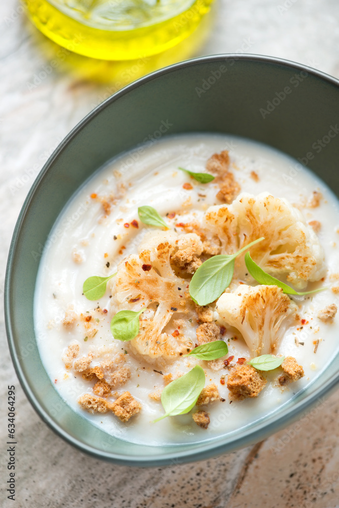 Middle close-up of cauliflower cream-soup served with roasted florets and croutons in a green bowl, vertical shot, selective focus Middle close-up of cauliflower cream-soup served with roasted florets and croutons in a green bowl, vertical shot, selective focus