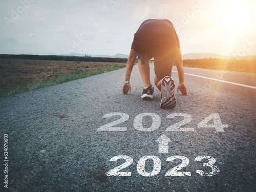 White arrow and text 2023 to 2024 on asphalt road A runner who is preparing to run forward entering the new year new beginning