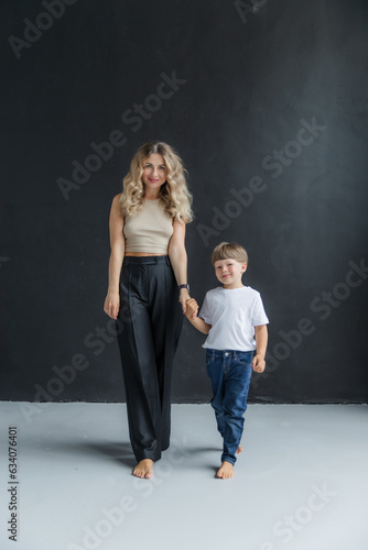 Mom and son at a photo shoot in the studio. Full length portrait in motion. Mom is wearing in a black pants. The boy is wearing a white T-shirt and jeans.Mom and son step forward synchronously.