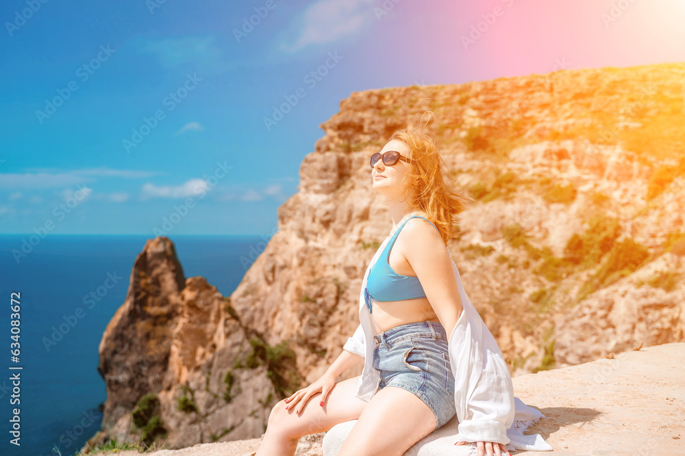 Woman travel summer sea. Portrait of a happy woman on a background of rocks and the sea. Side view of a woman in a white shirt and swimsuit. Freedom and happiness