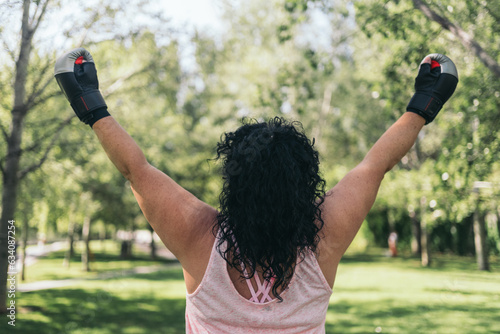 Female athlete with street boxing gloves on her back raising her arms in sign of victory after finishing her training.