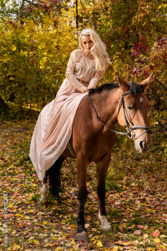 A woman in a long dress sits on a horse. Autumn forest, horse breeding