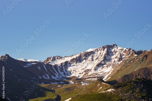 Large mountain range with steep slope and meadows at the foot