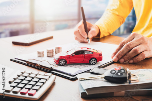 Car loan or buying a new car concept. Red car on clipboard and car key on table with a man signing on lease or document  form in background. Vehicle or automotive business finance concept. 