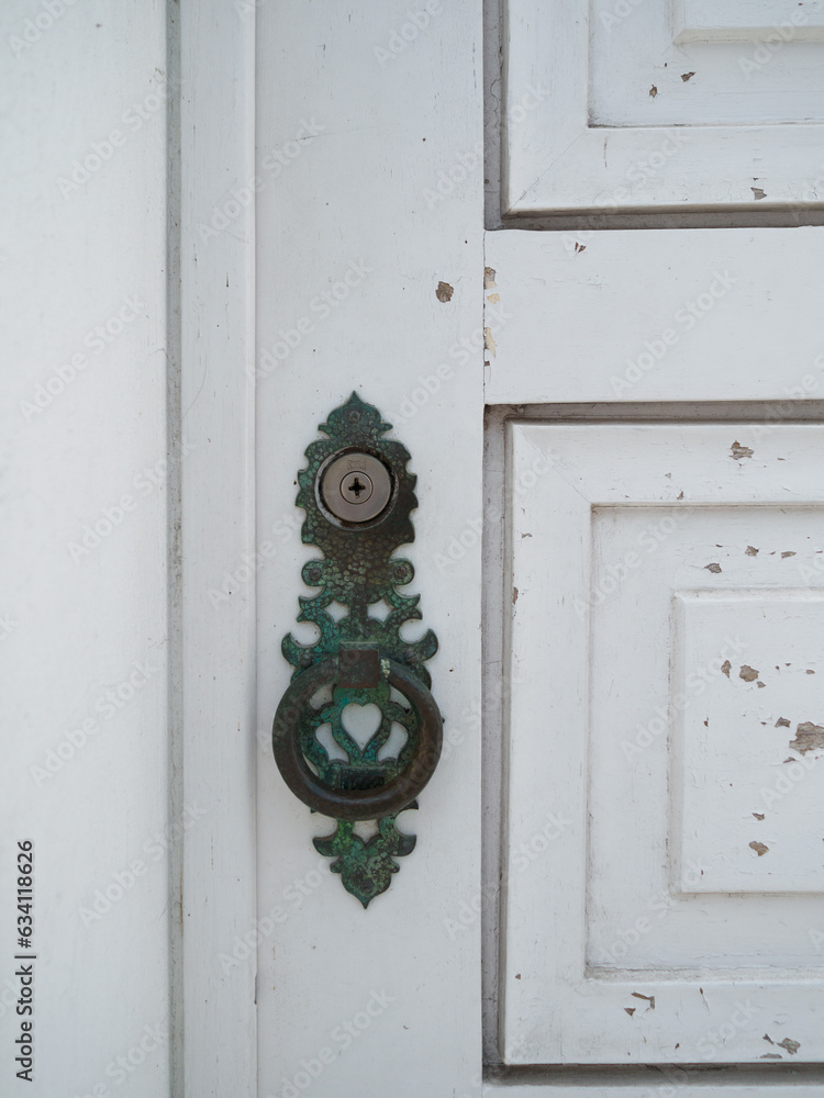 antique metal knob and green color that stands out against the worn white door. exterior building in Aveiro, Portugal.