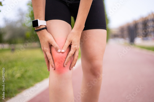 Sport workout injury. Female athlete holding knee in pain on running training outdoors.