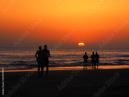 People on the background of a red sunset on the seashore.