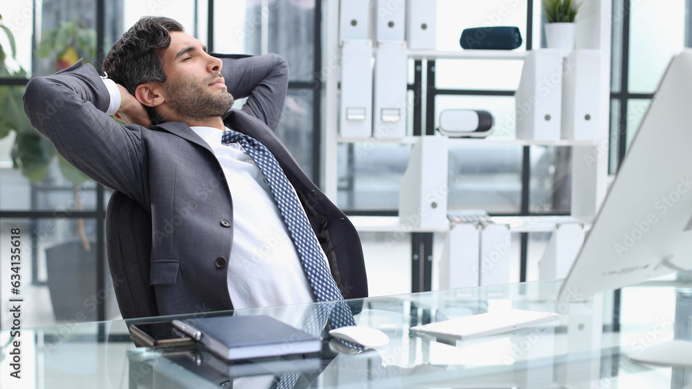 Fototapeta premium Cheerful young man holding hands behind head and keeping eyes closed while sitting at his working place