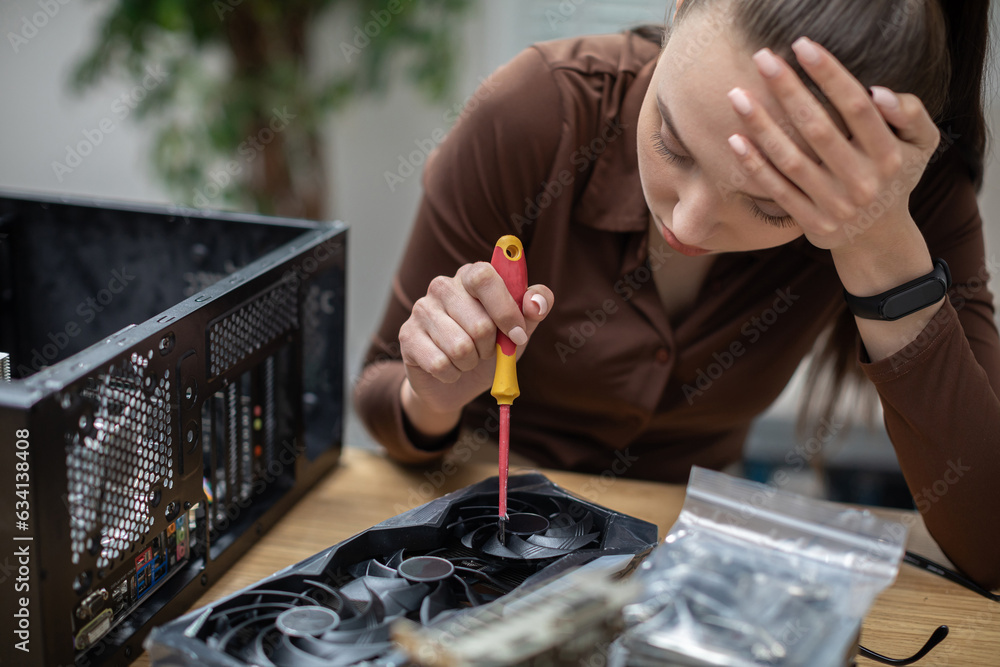Fototapeta premium A befuddled girl tries to fix a computer part with a screwdriver.