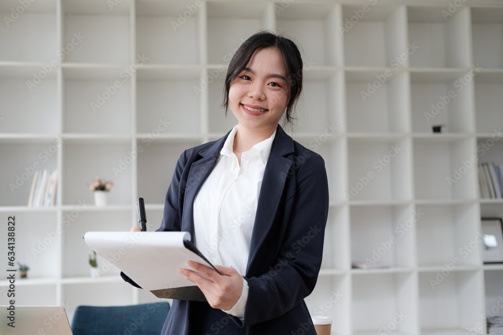 Professional Asian businesswoman holding working document while standing in the office room. Professional Asian businesswoman holding working document while standing in the office room.