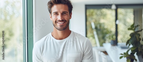 Portrait of a joyful young man holding tablet and smiling at camera by a window