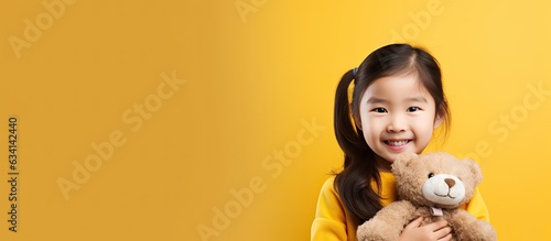 Print op canvas Cute Asian girl with teddy bear standing alone on yellow background