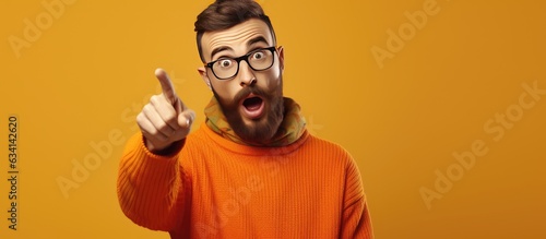 Shocked hipster guy in casual outfit pointing aside offering huge sale on orange studio background for banner design