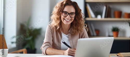 Smiling woman at desk using laptop and notebook studying online at home photo