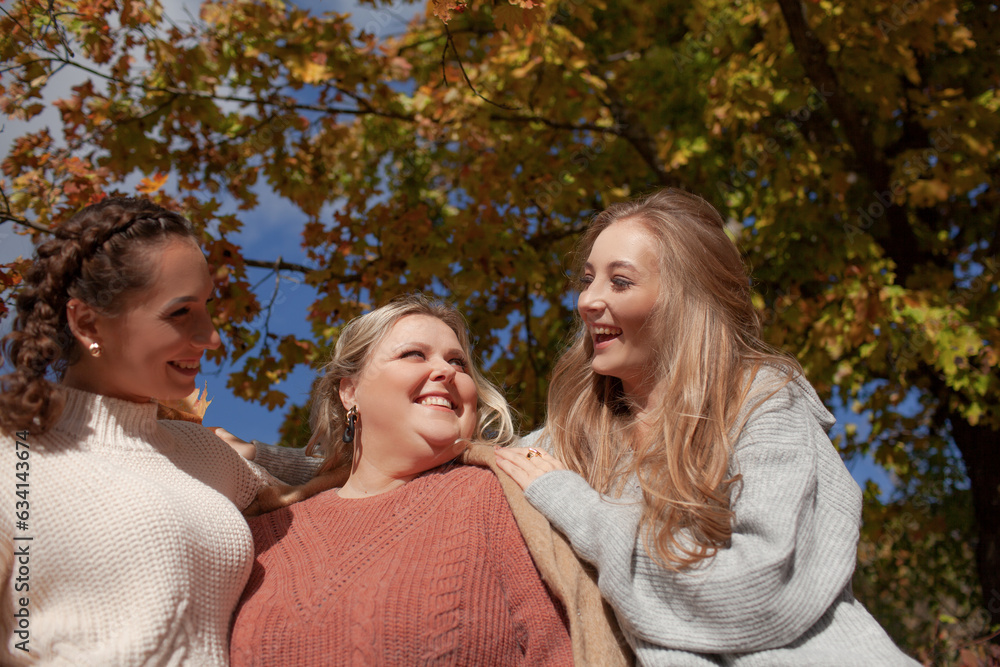 Fototapeta premium Multiracial female people with different bodies and hairs walking in the fall parks together. Friends wearing warm fashion clothes, knitted sweaters.