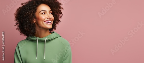 Curly woman in green sweater smiles happily standing alone on pink background